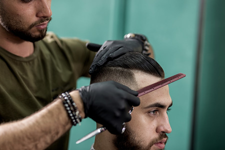 Barber in black gloves combs hair of stylish man at a barbershopの写真素材