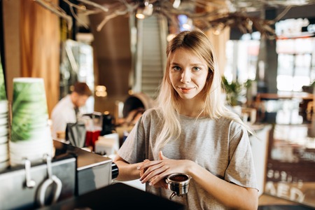 A pretty smiling slim girl,wearing casual clothes,holds some ground coffee and looks at the camera in a cozy coffee shop.の写真素材