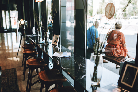 Tables with chairs are shown,situated next to a glass wall. Lovely atmosphere of the coffee shop is shownの写真素材