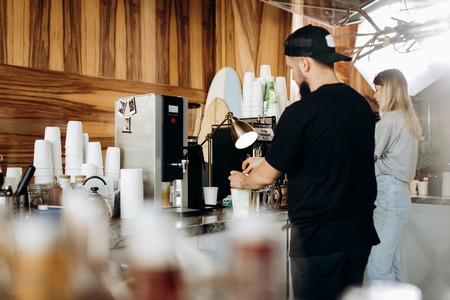 A young stylish man with beard,dressed i casual style,is cooking coffee in the expensive coffee machine in a cozy coffee shop.の写真素材