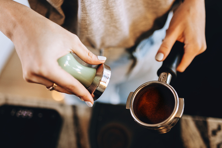 A young pretty slim girl,wearing casual outfit,is cooking coffee in a modern coffee shop. It focuses on the process.の写真素材