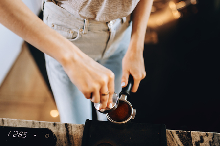 A young pretty slim girl,wearing casual outfit,is cooking coffee in a modern coffee shop. It focuses on the process.の写真素材