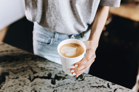 A youthful slim kind blonde girl,dressed in casual outfit,skillfully adds milk to coffee in a modern coffee shop.の写真素材