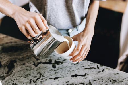 A youthful slim kind blonde girl,dressed in casual outfit,skillfully adds milk to coffee in a modern coffee shop.の写真素材
