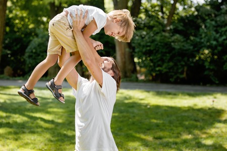 Sunny summer day. Cheerful father lifted his little son up above himself and tickling him.の写真素材