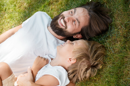 Joyful father and son are laying together on the green grass and laughing in a sunny day.の写真素材