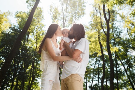 Happy family on the open air. Young dark-haired woman and her husband are kissing their charming...