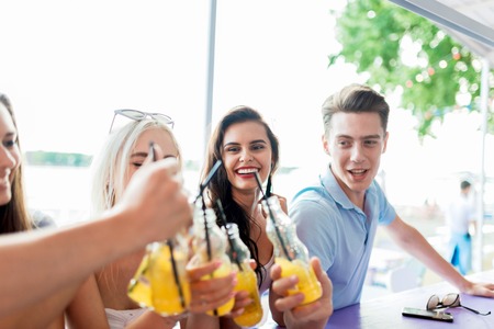 A company of good-looking friends laughing, drinking yellow cocktails and socialising at the bar in...