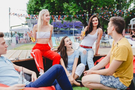A company of good-looking friends laughing, drinking yellow cocktails and socialising while sitting...