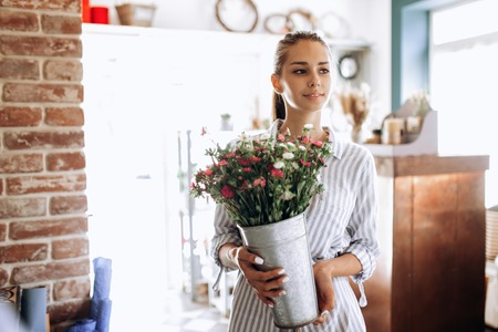 Beautiful brunette girl dressed in a striped dress holds a vase with pink and white chrysanthemums in the flower shopの写真素材