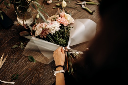 Florist cuts a ribbon on the bouquet of fresh flowers in pastel colors.