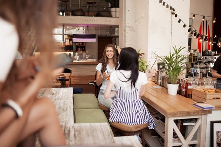 Two cute slim dark-haired girls,wearing casual style, sit opposite each other and chat in a cozy coffee shop.の写真素材