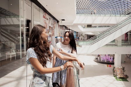 Two young cute thin dark-haired girls,stand next to each other in a modern mall.