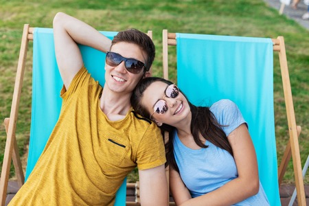 A beautiful couple in the sunglasses is lying on the deck chairs on the lawn in the nice summer cafe. Entertainment, having good time. Friendship, relationship.の写真素材