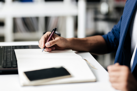 Man makes notes in a notebook on a table with a phoneの写真素材