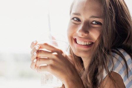 A young beautiful thin smiling girl with long hair,wearing casual style,is looking at the camera and holding a glass,の写真素材