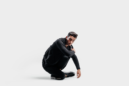 Dark-haired stylish dancer dressed in a stylish black clothes is sitting on the floorの写真素材