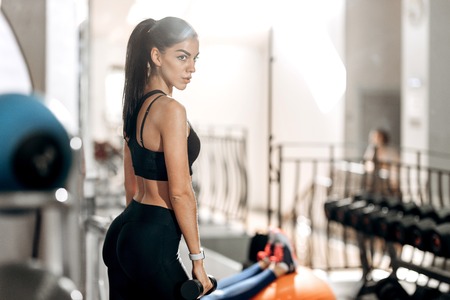 Athletic girl dressed in black sports top and tights holds dumbbells in her hands in the gymの写真素材