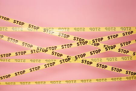 Pink wall with the yellow   tapes with inscriptions of word "stop" on itの写真素材