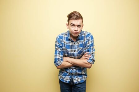 Pensive l guy dressed in a plaid shirt and jeans stands next to yellow wall in the studioの写真素材