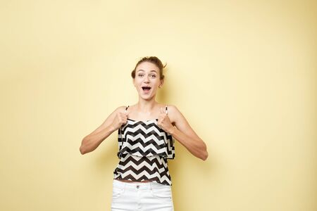 Ecstatic girl dressed in a striped top and white jeans happily shouts on the yellow background in the studioの写真素材