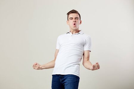 Full of energy joyful guy dressed in a white t-shirt and jeans happily shouts in the studio on a white backgroundの写真素材