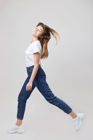 Happy girl dressed in a white t-shirt and jeans walks in the studio on a white backgroundの写真素材