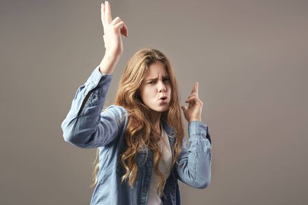 Nice girl with long brown hair dressed in a white t-shirt, jeans and jeans shirt fools around on a gray backgroundの写真素材
