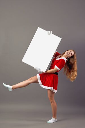 Young nice mrs.Santa Claus dressed in the red robe, white gloves and white socks  rises up a white canvas on the gray background.の写真素材