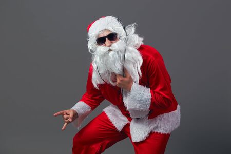 Santa Claus  with a long white beard in sunglasses and headphones stands shows a rock sing on the white background.の写真素材
