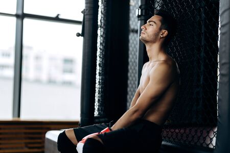 Sportsman with a naked torso and the red boxing gloves  on his hands  sits on the border of boxing ringの写真素材