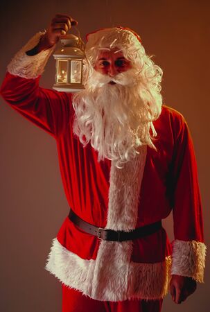 Santa Claus with a long white beard holds candle holder with burning candle on a beige background. Christmasの写真素材