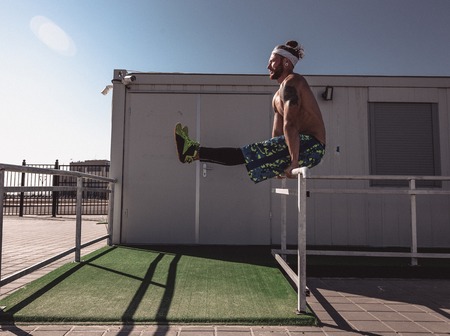 Young athletic man with a naked torso with tattoos and with headband dressed in the  black leggings...