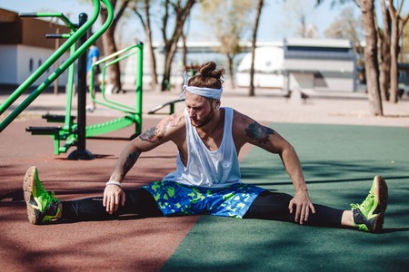 Athletic man with headband on his head and tattoos dressed in the white t-shirt, black leggings and...