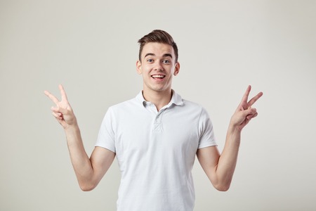 Happy  guy dressed in a white t-shirt and jeans shows  V sign with both hands on a white background in the studioの写真素材