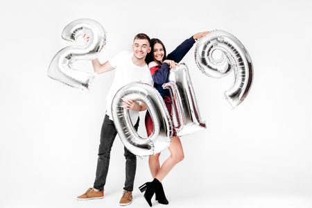 Funny girl and guy dressed in a stylish smart clothes are holding balloons in the shape of numbers 2019 on a white background in the studioの写真素材