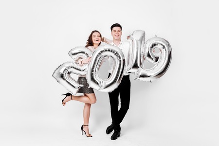 Happy girl and guy dressed in a stylish smart clothes are holding balloons in the shape of numbers...