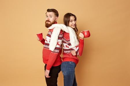 Girl and a guy dressed in red and white sweaters with deer and white knitted scarf  stand back to...