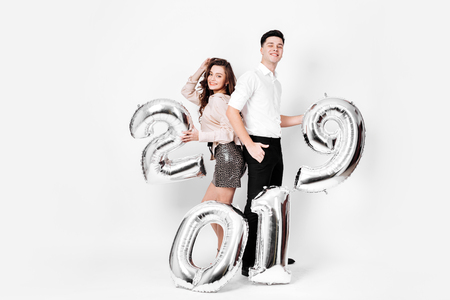 Girl and guy dressed in a stylish smart clothes are holding balloons in the shape of numbers 2019 on a white background in the studioの写真素材