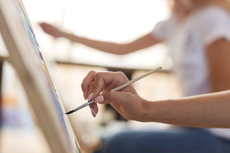 Girls hand holds a paint brush. Process of painting picture at the easels in the art studioの写真素材