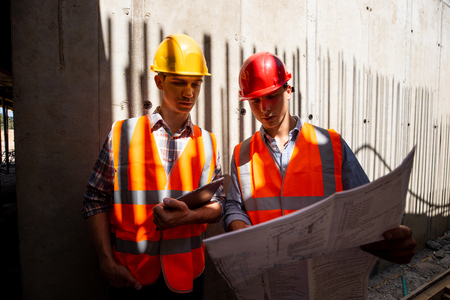 Two civil engineers dressed in orange work vests and helmets explore project documentation on the...