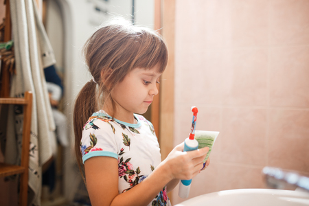 Little girl is standing in the bathroom holding a toothpaste and a toothbrushの写真素材