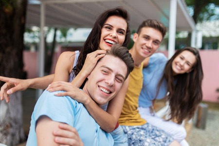 A company of good-looking friends is laughing and sitting on the railing in the nice summer cafe. Entertainment, having good time. Friendship.の写真素材