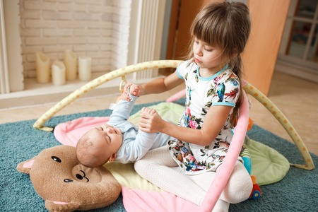 Little charming girl holds hands her tiny brother lying on the carpet on the floor in the roomの写真素材