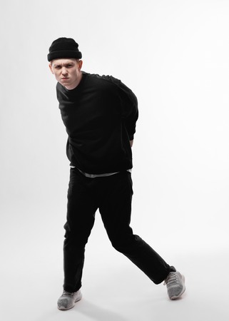 Young freestyle dancer dressed in black jeans, sweatshirt, hat and gray sneakers is dancing in the studio on the white backgroundの写真素材