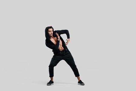 Young handsome young dancer dressed in black pants, a sweatshirt on a naked torso is dancing street dance. He makes stylized movements with his handsの写真素材