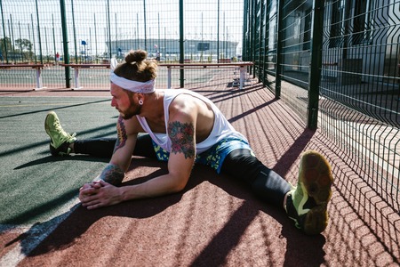 Athletic guy with white headband, dressed in the white t-shirt, black leggings and blue shorts doing...
