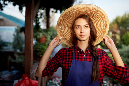 Charming girl gardener in a straw hat is standing in the wonderful garden on a sunny day.の写真素材