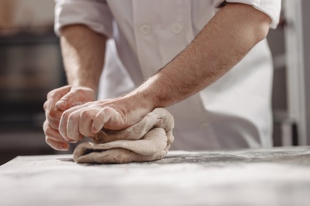 Baker  kneads  dough on the table in the bakeryの写真素材