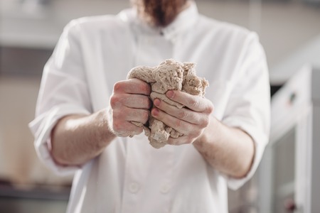 Professional baker kneads dough in his hands in the kitchen of the bakeryの写真素材